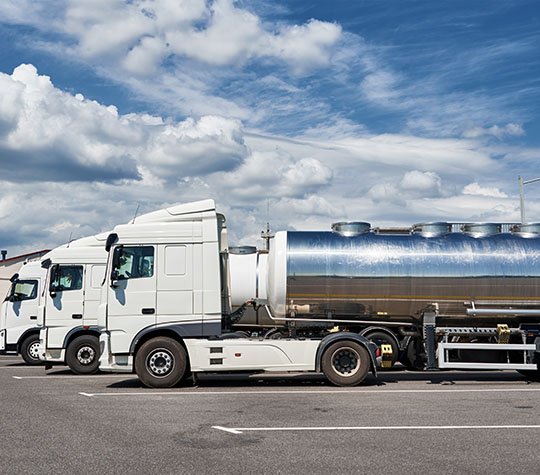 Two white trucks with tank trailers parked under a cloudy blue sky.