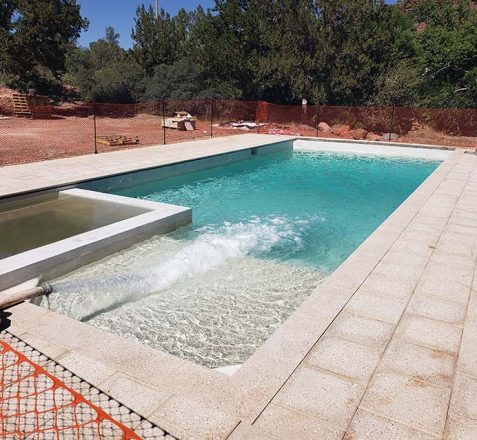 Outdoor swimming pool with adjacent empty spa under construction, surrounded by a safety fence.