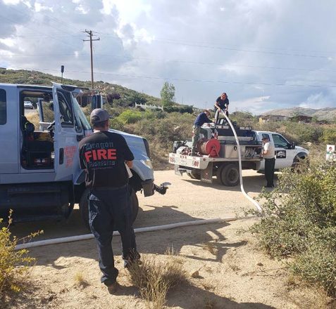 Firefighters preparing equipment near trucks on a sunny day with cloudy skies.