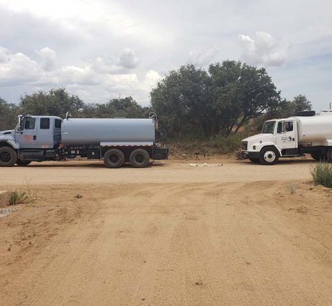 Two tank trucks on a sandy lot with trees in the background.