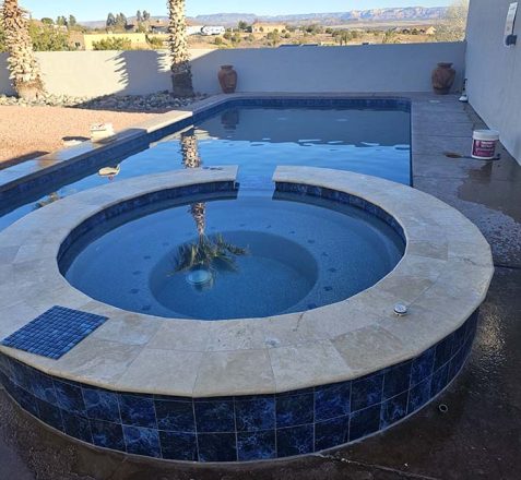 Backyard with a circular spa overflowing into a rectangular pool, desert landscape visible in the background.