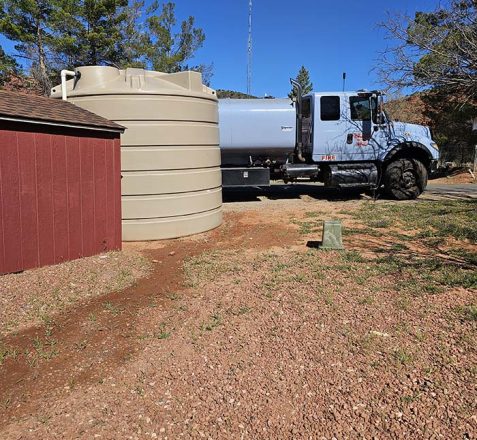 A water tank and a fire truck parked near trees under a clear blue sky.