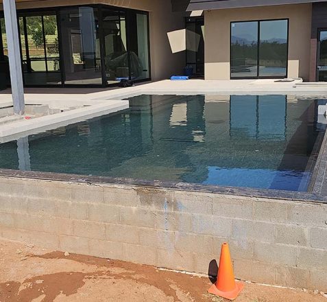 A newly constructed outdoor swimming pool beside a modern building, unfinished with raw concrete sides.