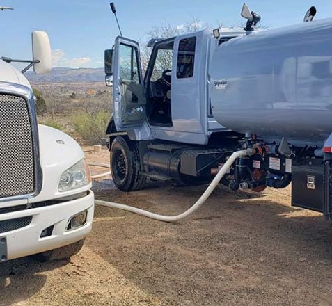 White tanker truck being filled from a fuel tank on a sunny day.